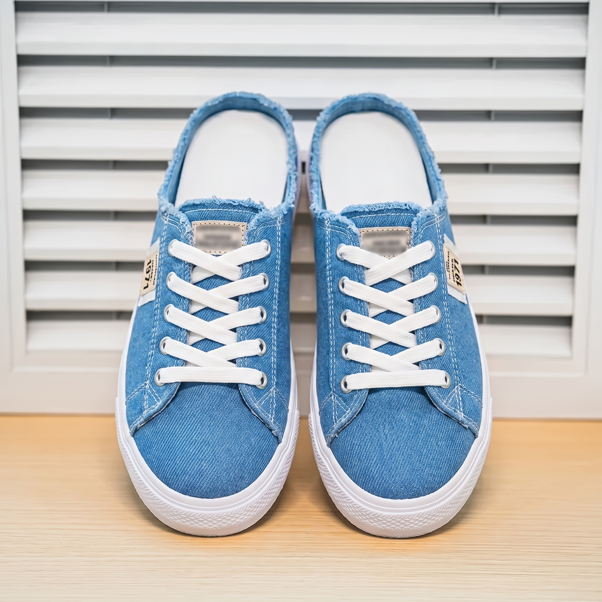 Zapatillas Mule Denim Premium sobre fondo de persiana blanca